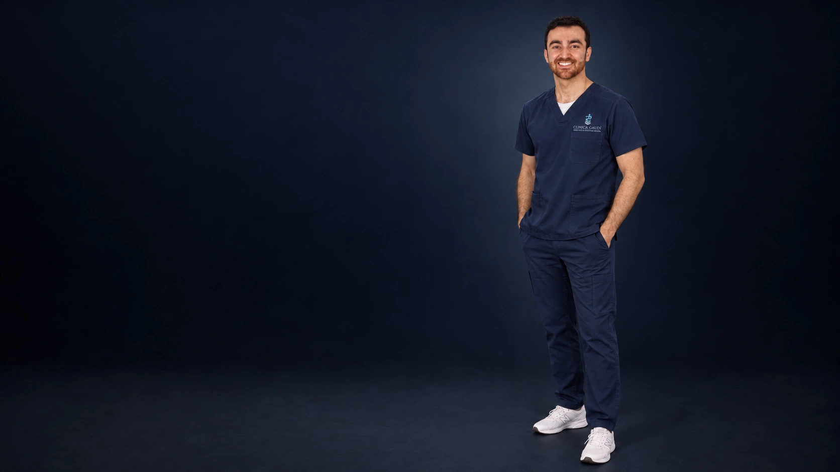 Retrato del Dr. Albert Ferré, odontólogo y director médico de Clínica Dental Gaudí, de cuerpo entero en un estudio fotográfico sobre fondo azul noche.